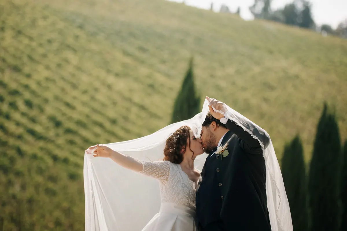 A couple kissing beneath a lifted veil on a green hillside