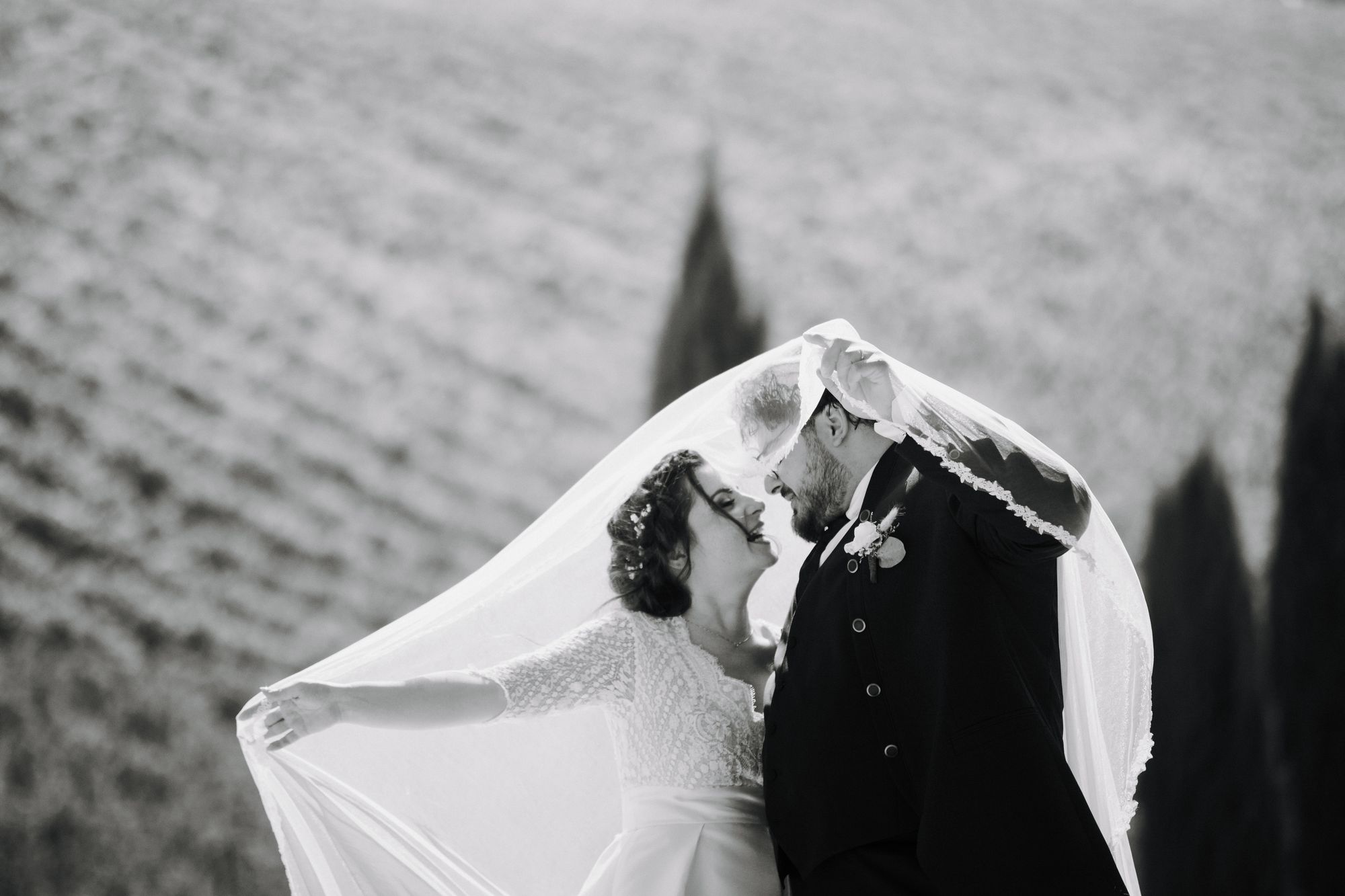 A black and white frame of a couple kissing beneath a veil