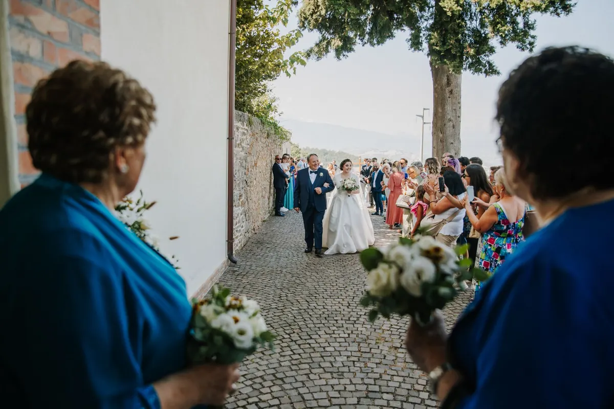 Guests holding bouquets as the couple walk a cobbled lane after the ceremony